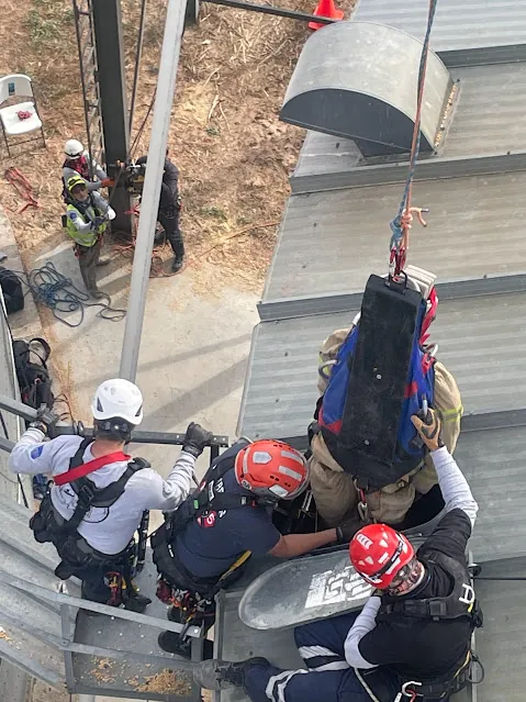Vista desde arriba: rescatistas extraen por la escotilla de un silo a una víctima empaquetada.